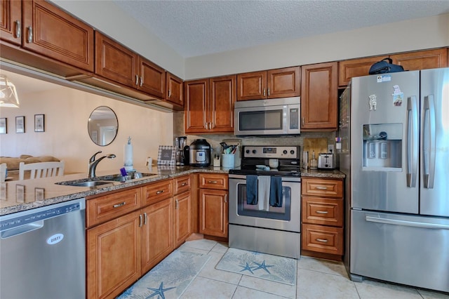 kitchen with a textured ceiling, light stone countertops, sink, and appliances with stainless steel finishes