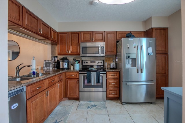 kitchen featuring sink, stainless steel appliances, dark stone counters, a textured ceiling, and light tile patterned floors