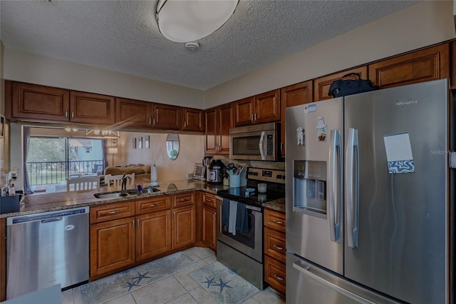 kitchen featuring sink, dark stone countertops, light tile patterned floors, a textured ceiling, and appliances with stainless steel finishes