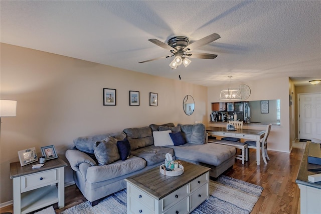 living room featuring ceiling fan with notable chandelier, dark hardwood / wood-style flooring, and a textured ceiling