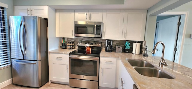 kitchen with appliances with stainless steel finishes, white cabinetry, light stone counters, backsplash, and sink