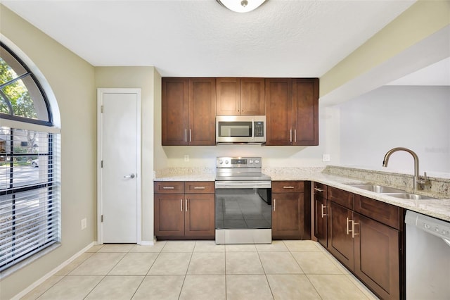 kitchen with appliances with stainless steel finishes, light stone countertops, light tile patterned floors, a textured ceiling, and sink