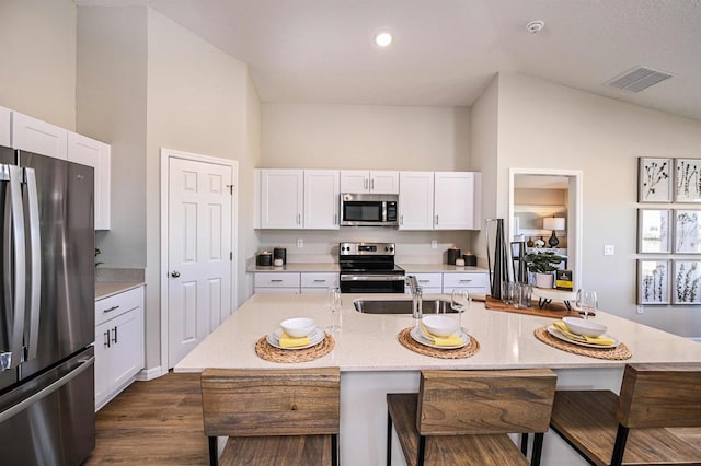 kitchen featuring an island with sink, stainless steel appliances, white cabinets, and vaulted ceiling