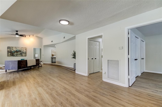 unfurnished living room with ceiling fan, vaulted ceiling, a textured ceiling, and light hardwood / wood-style floors