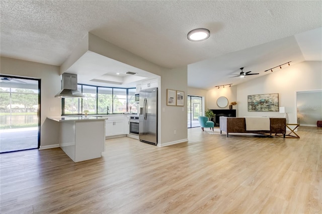 kitchen with white cabinets, wall chimney range hood, light hardwood / wood-style flooring, appliances with stainless steel finishes, and ceiling fan