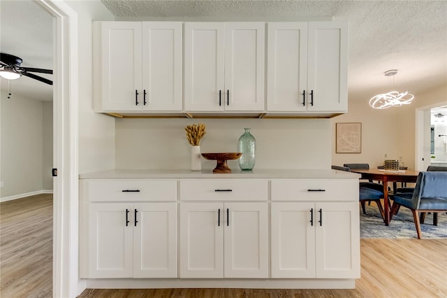 interior space featuring light hardwood / wood-style floors, white cabinetry, ceiling fan with notable chandelier, pendant lighting, and a textured ceiling