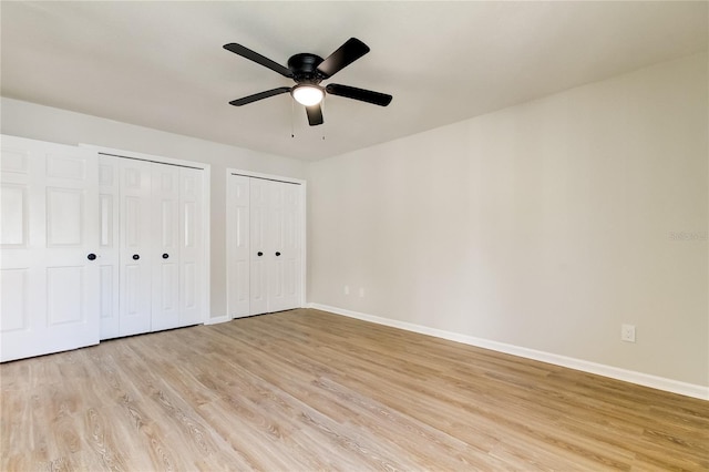 unfurnished bedroom with light wood-type flooring, ceiling fan, and multiple closets