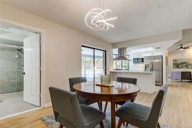 dining area with a textured ceiling, ceiling fan with notable chandelier, and light wood-type flooring