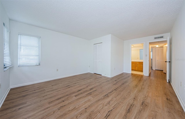 unfurnished bedroom with a textured ceiling, connected bathroom, light hardwood / wood-style floors, and a closet