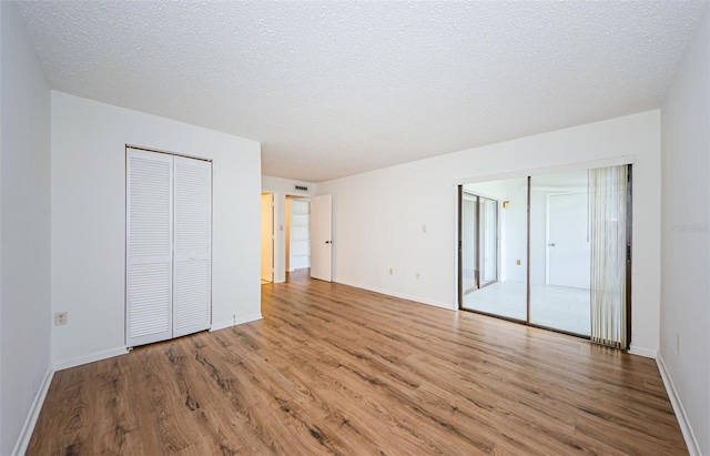 unfurnished bedroom featuring a textured ceiling, hardwood / wood-style floors, and multiple closets