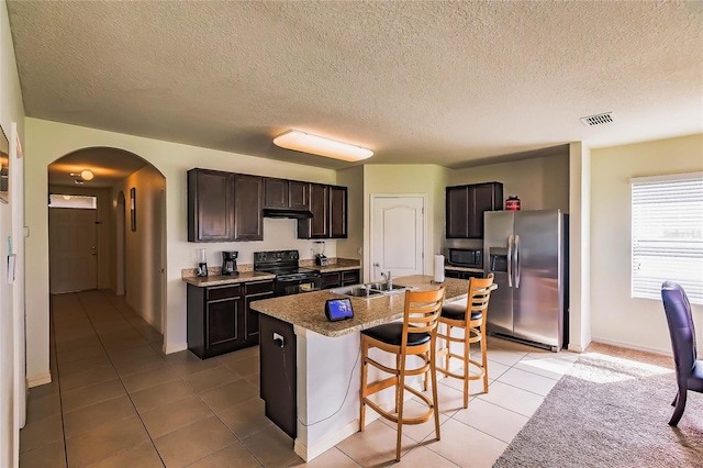 kitchen with black appliances, a kitchen breakfast bar, a center island with sink, dark brown cabinets, and light tile patterned flooring