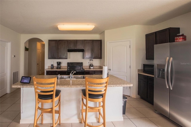 kitchen with sink, an island with sink, a breakfast bar, light tile patterned flooring, and black appliances