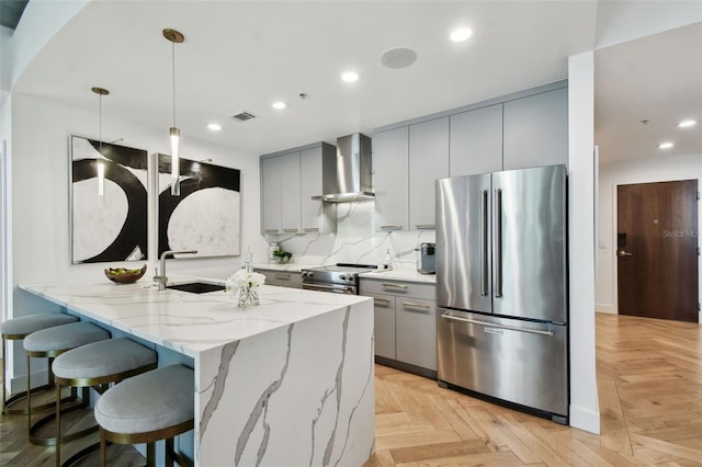 kitchen featuring light parquet flooring, wall chimney exhaust hood, kitchen peninsula, pendant lighting, and stainless steel appliances