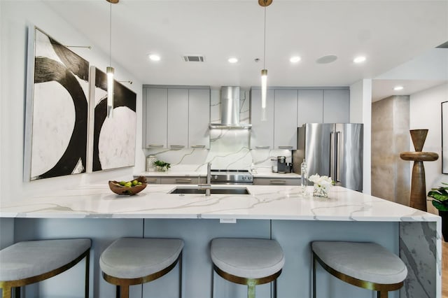 kitchen featuring appliances with stainless steel finishes, gray cabinetry, a breakfast bar area, decorative light fixtures, and wall chimney range hood