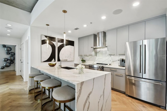 kitchen featuring hanging light fixtures, light stone counters, wall chimney exhaust hood, kitchen peninsula, and stainless steel appliances