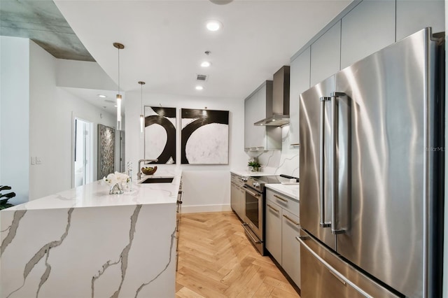 kitchen featuring pendant lighting, sink, wall chimney exhaust hood, appliances with stainless steel finishes, and light stone countertops