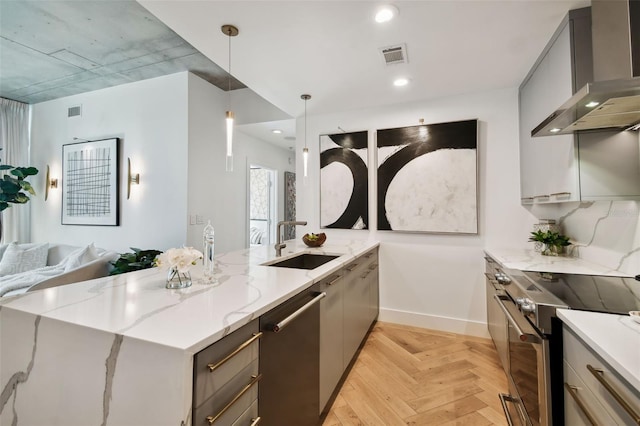 kitchen with light stone counters, gray cabinetry, decorative light fixtures, wall chimney exhaust hood, and stainless steel appliances