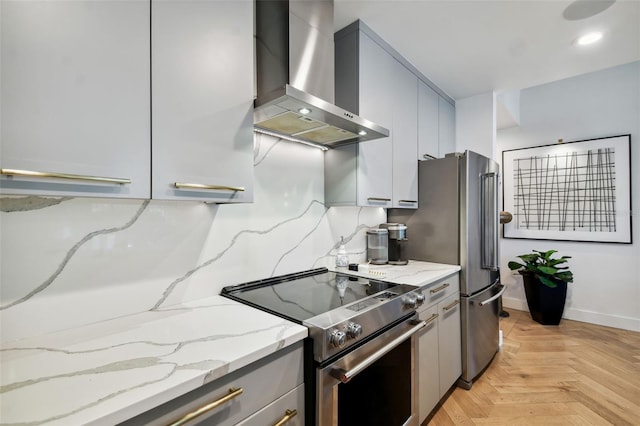 kitchen featuring gray cabinets, light stone counters, electric stove, wall chimney range hood, and light parquet flooring