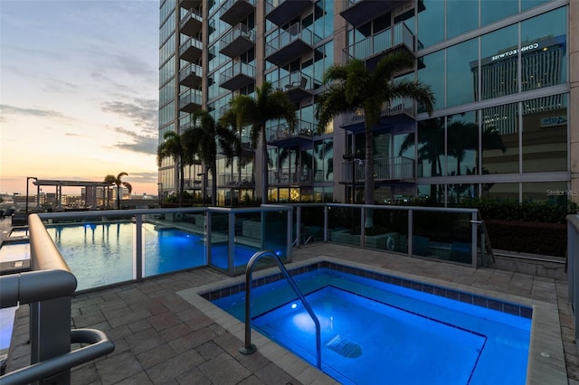 pool at dusk with a hot tub