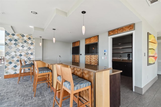 kitchen with pendant lighting, sink, kitchen peninsula, stone counters, and a kitchen breakfast bar