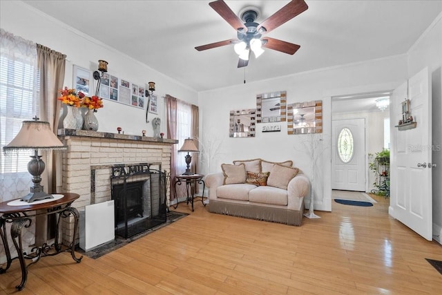 living room featuring a brick fireplace, wood-type flooring, ceiling fan, and crown molding