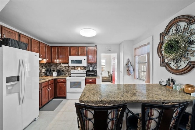 kitchen with a breakfast bar area, kitchen peninsula, decorative backsplash, white appliances, and light stone countertops