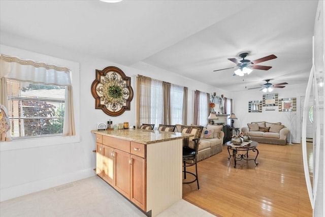 kitchen featuring ceiling fan, light stone counters, a breakfast bar, light brown cabinetry, and light hardwood / wood-style floors