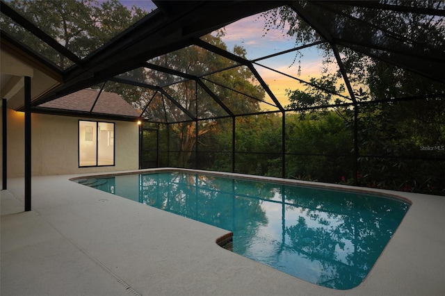 pool at dusk featuring glass enclosure and a patio