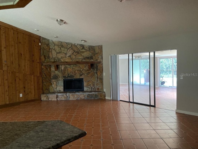 unfurnished living room with tile patterned flooring, wood walls, a textured ceiling, and a stone fireplace