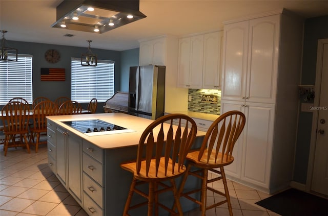 kitchen featuring black electric cooktop, stainless steel fridge, white cabinetry, and pendant lighting