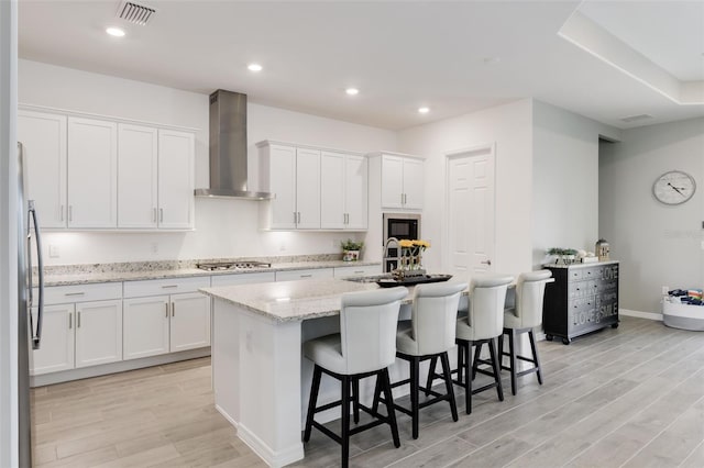 kitchen featuring wall chimney exhaust hood, white cabinetry, and an island with sink