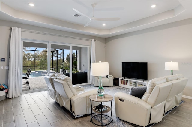 living room featuring light hardwood / wood-style floors, a tray ceiling, and ceiling fan