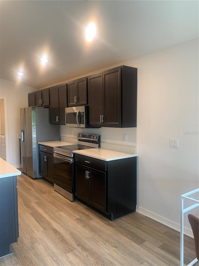 kitchen with dark brown cabinets, stainless steel appliances, and light wood-type flooring