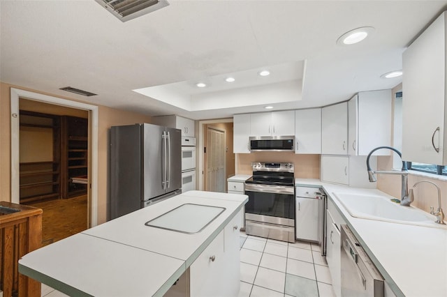 kitchen with appliances with stainless steel finishes, a raised ceiling, sink, light tile patterned floors, and white cabinetry