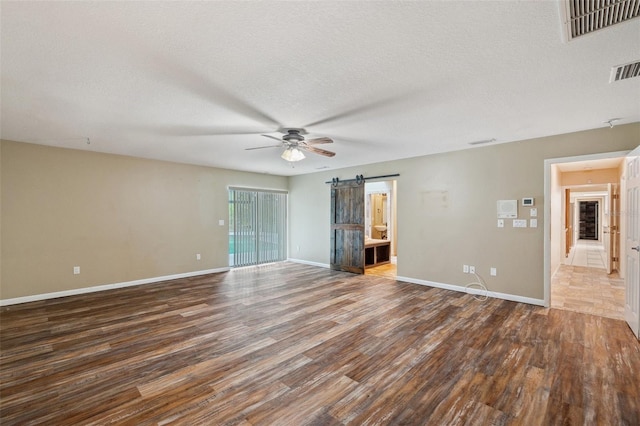 spare room with wood-type flooring, a barn door, a textured ceiling, and ceiling fan