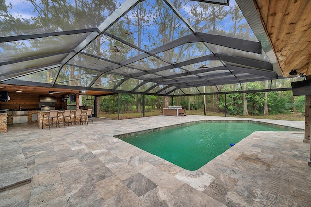 view of pool with glass enclosure, an outdoor bar, an outdoor kitchen, and a patio