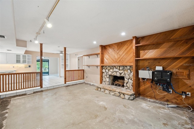 unfurnished living room featuring a fireplace, a textured ceiling, concrete floors, and wood walls