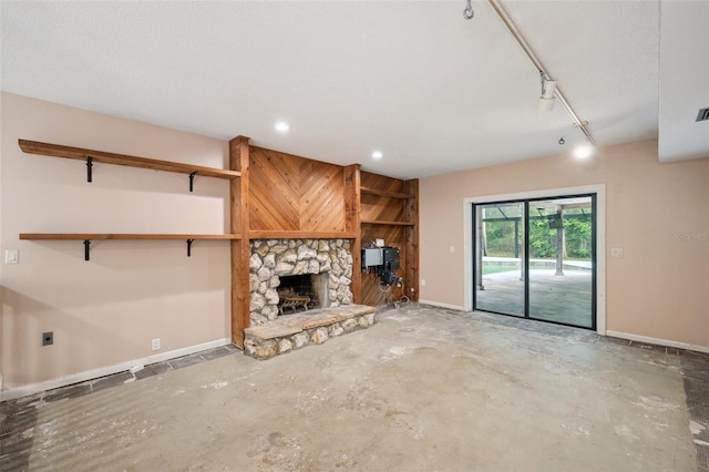 unfurnished living room featuring concrete floors, a fireplace, and track lighting