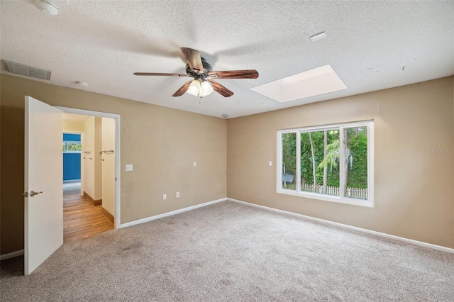 spare room featuring a skylight, a textured ceiling, light colored carpet, and ceiling fan