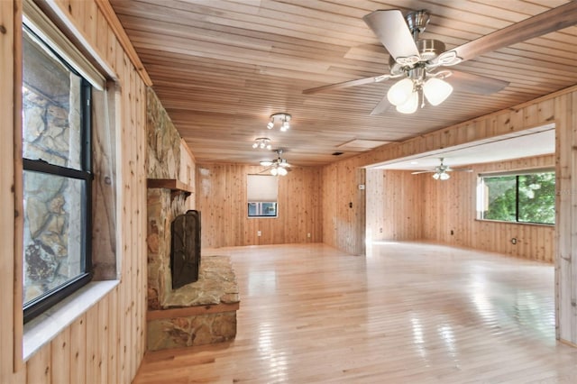 unfurnished living room featuring light wood-type flooring, ceiling fan, wooden walls, wooden ceiling, and a fireplace