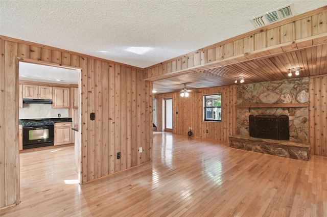 unfurnished living room featuring ornamental molding, ceiling fan, light hardwood / wood-style flooring, a fireplace, and wood walls