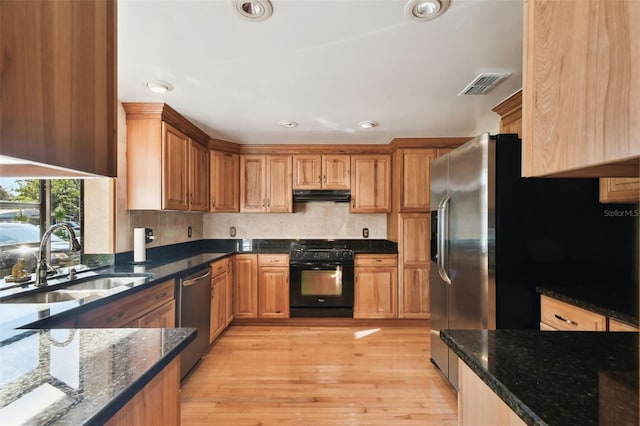 kitchen featuring light wood-type flooring, sink, appliances with stainless steel finishes, and dark stone counters