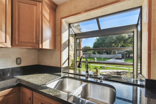 kitchen with decorative backsplash, dark stone countertops, a healthy amount of sunlight, and sink