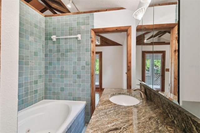 bathroom with vaulted ceiling with beams, a relaxing tiled tub, a textured ceiling, and vanity