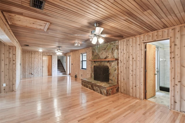 unfurnished living room with wood walls, light wood-type flooring, wooden ceiling, and a fireplace