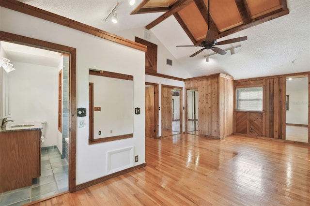 unfurnished room featuring a textured ceiling, ceiling fan, sink, vaulted ceiling with beams, and light hardwood / wood-style floors