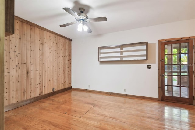 spare room with wooden walls, ceiling fan, and light wood-type flooring