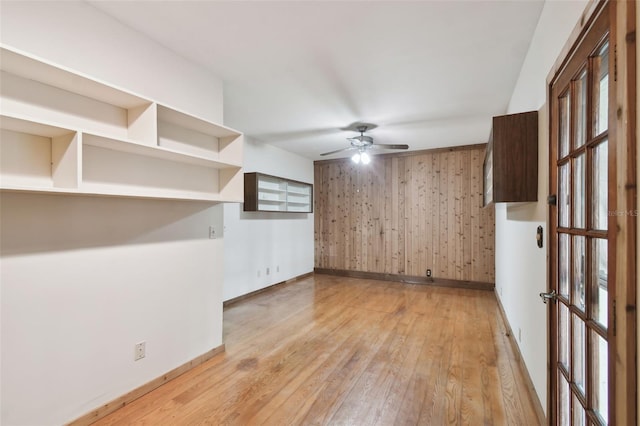 unfurnished room with light hardwood / wood-style flooring, ceiling fan, and wood walls