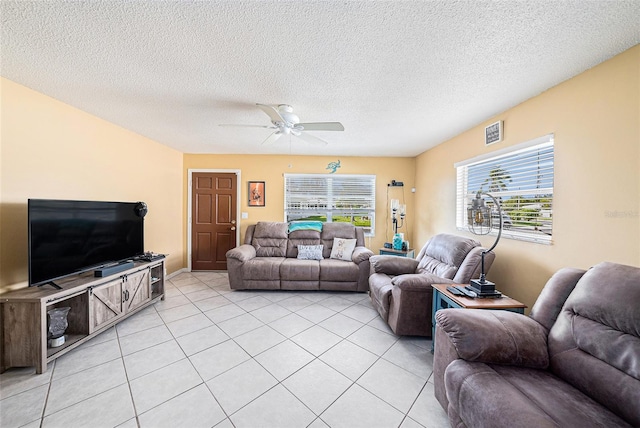 living room with light tile patterned flooring, visible vents, ceiling fan, and a textured ceiling