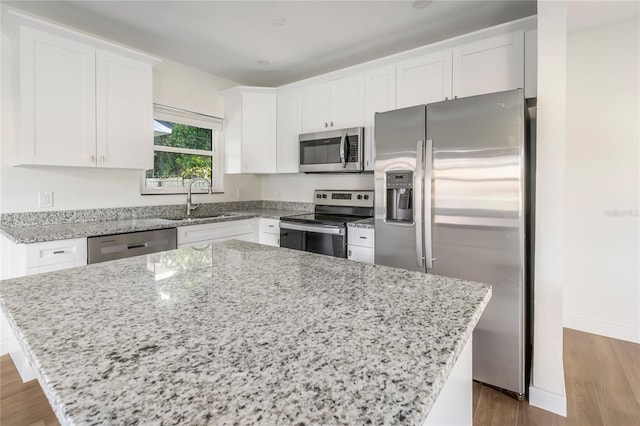 kitchen with appliances with stainless steel finishes, light stone counters, white cabinets, a kitchen island, and wood-type flooring